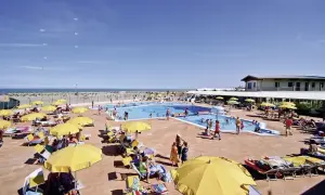 Sonnige Poolanlage mit vielen Liegen und gelben Sonnenschirmen am Rosapineta Sud. Kinder planschen im Wasser, während Möwen über dem Meer kreisen.