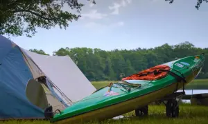 Grünes Kajak mit Schwimmweste auf einem Anhänger neben einem Zelt. Perfekte zelt gadgets für ein Abenteuer am See.