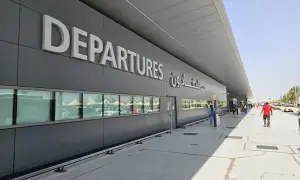 Große "DEPARTURES" Schriftzüge am Flughafen Dubai Terminal 3. Menschen und Autos spiegeln sich in den Fenstern.