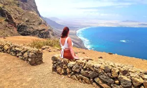 Frau genießt ihren Urlaub alleine auf einem Felsvorsprung mit Blick auf das türkisfarbene Meer und die Küste.
