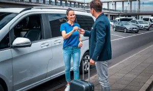 Mann übergibt Schlüssel an Frau neben weißem Van. Das bedeutet Valet-Service: bequemes Parken am Flughafen.