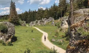 Frau wandert auf einem Kiesweg durch eine felsige Landschaft mit grünen Wiesen und Bäumen. Perfekt für einen entspannten outdoor urlaub.