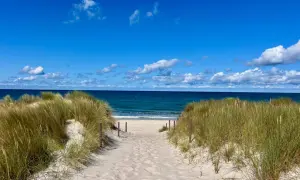 Sandiger Weg durch Dünen zum blauen Meer. Perfekter Urlaub am Meer mit Sonnenschein und Wolken.