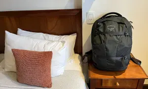 Schwarzer Osprey-Rucksack neben einem Bett mit Kissen. Perfekt für deine Packliste Mexiko.