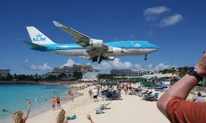 Ein KLM-Flugzeug landet tief über dem Maho Beach Flughafen. Urlauber am Strand winken dem Jumbo-Jet zu.