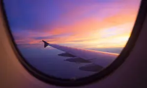 Flugzeugfenster mit Flügel und einem atemberaubenden Sonnenuntergang in Violett- und Orangetönen. Perfekt, um einen **stopover flug buchen** zu planen.