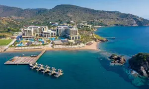 Luftaufnahme des Sune Efes Royal Palace mit Pools, Wasserrutschen und einem Steg mit Liegen am türkisfarbenen Meer.