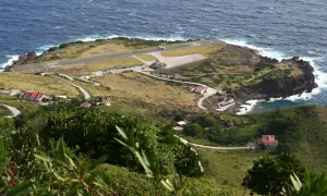 Ein Flugzeug landet auf der Landebahn des kleinsten Flughafens der Welt, umgeben von grünen Hügeln und dem blauen Meer.