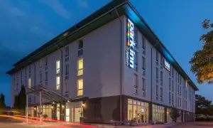 Das Park Inn Wien bei Nacht, beleuchtet mit bunten Lichtern. Autos fahren vorbei und hinterlassen rote Lichtspuren.