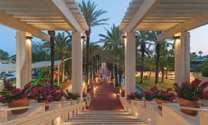Ein beleuchteter Weg mit Palmen führt zum Seven Seas Hotel. Blumenkästen säumen die Treppe.