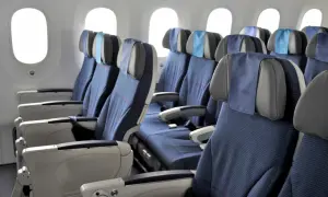 Reihe von blauen Flugzeugsitzen mit Kopfstützen und Armlehnen, daneben Fenster. Ein Fensterplatz im Flugzeug bietet Aussicht.