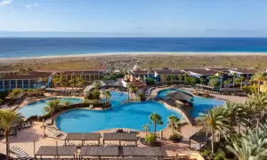 Ein Urlaubsparadies am Meer: Große Poollandschaft mit Palmen und Liegen, dahinter das Robinson Jandia Playa Resort und der weite Sandstrand.