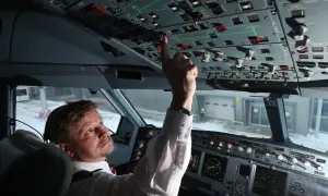 Pilot im Cockpit prüft die Anzeigen. Er bedient einen Schalter, während draußen Schnee liegt.