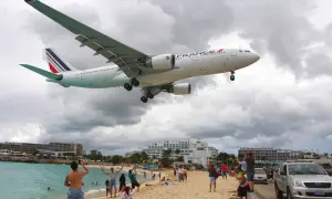 Air France Flugzeug landet auf einem Flughafen direkt am Strand. Menschen amüsieren sich am Meer, während das Flugzeug über sie hinwegfliegt.