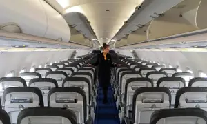 Flugbegleiterin in einem leeren Flugzeug. Die Reihen von Sitzen und die sorgfältige Präsentation lassen die Frage "Ist Lufthansa sicher?" positiv beantworten.