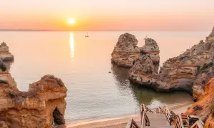Sonnenuntergang an der Algarve: Ein perfekter Urlaub in Portugal am Meer mit Felsformationen und einer Holztreppe zum Strand.