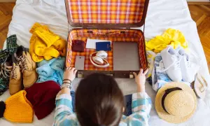 Packliste Mallorca: Koffer wird mit Kleidung, Schuhen, Kopfhörern, Reisepass und Laptop gepackt.