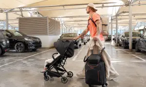 Mann mit Gepäck und Kinderwagen auf dem Parkplatz eines Flughafens.