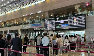 Menschen stehen in einer Schlange am Flughafen Seoul vor einer Anzeigetafel mit Abflugzeiten.