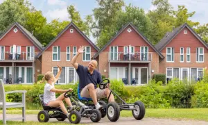 Vater und Tochter winken fröhlich, während sie mit Go-Karts durch die Anlage des TUI Kids Club fahren.