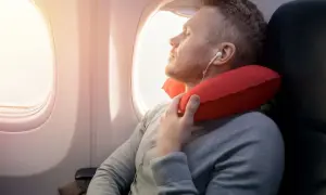 Mann schläft im Flugzeug mit rotem Nackenkissen. Ein Nackenkissen Flugzeug ist sinnvoll für bequemen Schlaf.