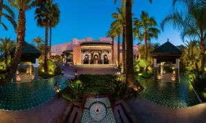 Eingangsbereich des La Mamounia Hotels in Marrakesch bei Dämmerung, umgeben von Palmen und beleuchteten Pavillons.