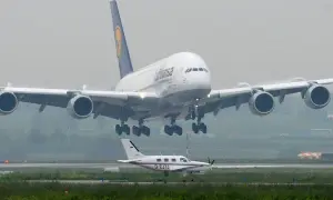 Ein riesiger A380 von Lufthansa landet, sein enormes Gewicht wird durch die vier Triebwerke und das Fahrwerk sichtbar. Ein kleines Propellerflugzeug wartet daneben.