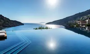 Infinity-Pool mit Blick auf die Bucht von Daios. Sonnenschein spiegelt sich im Wasser, Häuser schmiegen sich an den Hang.
