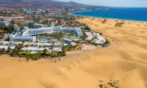 Das Riu Palace Maspalomas thront majestätisch am Rande der goldenen Dünen, mit dem blauen Meer im Hintergrund.