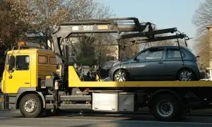 Gelber Abschleppwagen mit grauem Kleinwagen auf der Ladefläche. Ein unerwarteter Stopp, die abschleppkosten 400 euro sind ärgerlich.