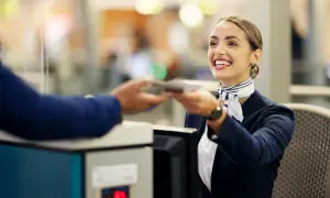 Lächelnde Flugbegleiterin am Schalter reicht einen Pass zurück. Ein Beispiel für Flughafen-Begriffe im Einsatz.