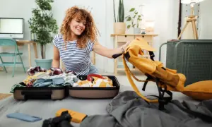 Frau packt Koffer für ihr Auslandssemester. Die Auslandssemester Packliste ist fast komplett, nur noch der gelbe Rucksack fehlt.