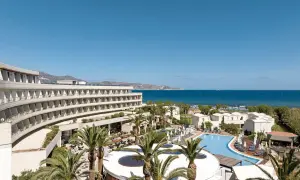 Agapi Beach Resort mit geschwungener Architektur, Pool und Palmen am Meer.