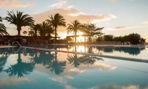 Sonnenuntergang am Robinson Esquinzo Playa. Palmen spiegeln sich im Pool.
