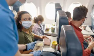 Fliegen mit FFP2-Maske: Eine Frau erhält ihr Essen im Flugzeug. Andere Passagiere tragen ebenfalls Masken.