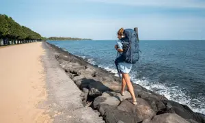 Frau mit großem Rucksack wandert über Felsen am Meer. Perfekte Packliste für Bali!