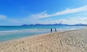 Traumhafter Strand auf Mallorca mit türkisfarbenem Meer und sanften Wellen. Zwei Personen genießen ihren Urlaub.