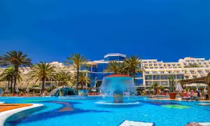 Einladender Poolbereich mit Wasserrutsche und Palmen vor dem Costa Calma Palace Hotel.