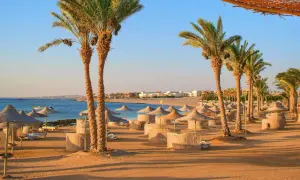 Sonnige Strandkulisse in Hurghada mit Palmen, Sonnenschirmen und Liegen. Perfekt für die Packliste Hurghada!