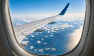Flugzeugfenster mit Blick auf Flügel, Wolken und Küste. Ein Gabelflug ist eine Reise mit zwei Zielen.
