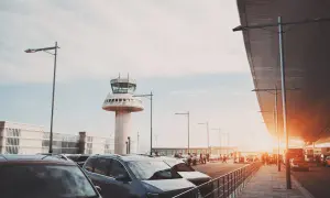 Autos parken am Flughafen Barcelona, mit dem markanten Kontrollturm im Hintergrund.