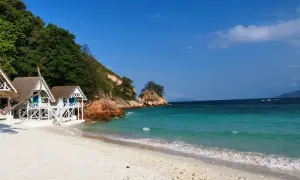 Traumhafte weiße Sandstrände und türkisfarbenes Wasser auf Rawa Island. Kleine weiße Hütten stehen am Ufer, umgeben von üppiger Vegetation und Felsen.