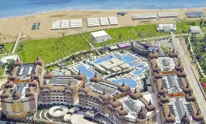 Luftaufnahme eines luxuriösen Resorts mit Kuppeldächern, Pools und Wasserrutschen, das an einen Strand grenzt. Ein Hauch von royal alhambra palace.