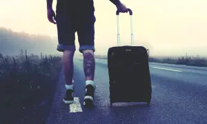 Mann mit Koffer auf einsamer Straße, bereit für London. Die Packliste ist komplett, das Abenteuer beginnt.