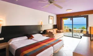 Gemütliches Zimmer im SBH Monica Beach Resort mit Meerblick. Zwei Betten, Sofa und Balkon laden zum Entspannen ein.