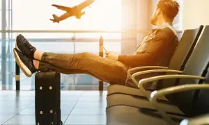 Mann mit Füßen auf Koffer wartet im Flughafen auf seinen Langstreckenflug. Ein Flugzeug hebt ab.