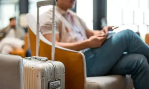 Mann mit Koffer im Wartebereich, bereit für die Dienstreise. Die Packliste für die Dienstreise ist vollständig.