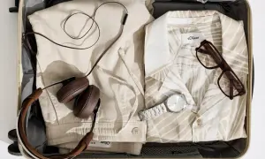 Koffer packen Liste Frauen: Leinenhose, gemustertes Hemd, Kopfhörer, Brille und Uhr für den perfekten Urlaub.