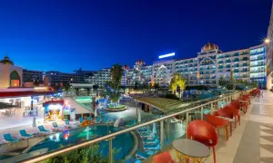 Abendansicht des Alan Xafira Deluxe Resort & Spa mit beleuchteten Pools, Palmen und stilvollen roten Stühlen auf der Terrasse.