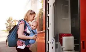 Frau mit Baby im Tragetuch steigt in den Zug. Abenteuerliches Backpacking mit Baby beginnt.